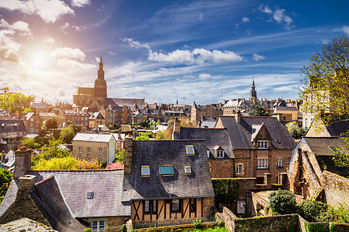 Beautiful view of scenic narrow alley with historic traditional houses and cobbled street in an old town of Dinan with blue sky and clouds. Brittany (Bretagne), France