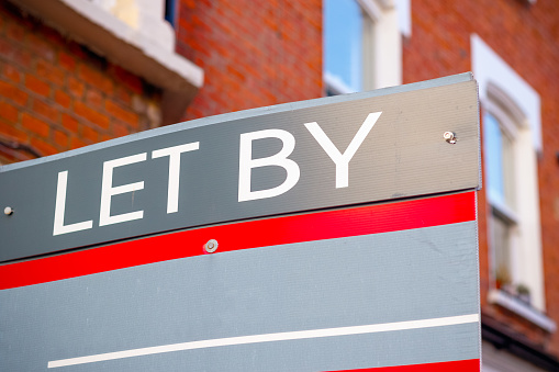 LET BY sign displayed on London street with traditional English terraced houses in the background