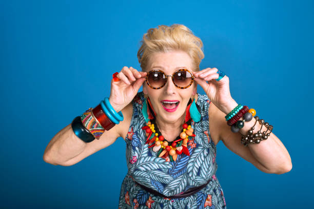 Summer portrait of young at heart senior woman Summer portrait of creative, colorful senior woman against blue background. Studio shot. middle aged woman fashion stock pictures, royalty-free photos & images