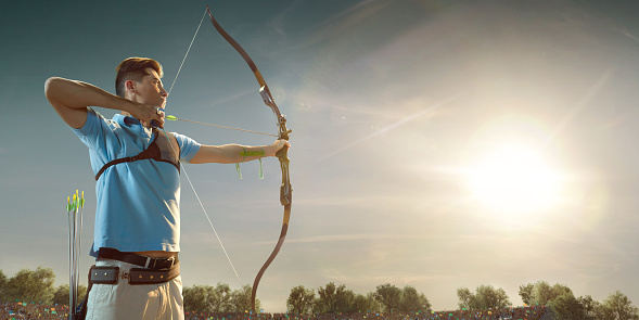 Male archer shooting with the longbow at sunset. Archer in professional field with a lot of fans.