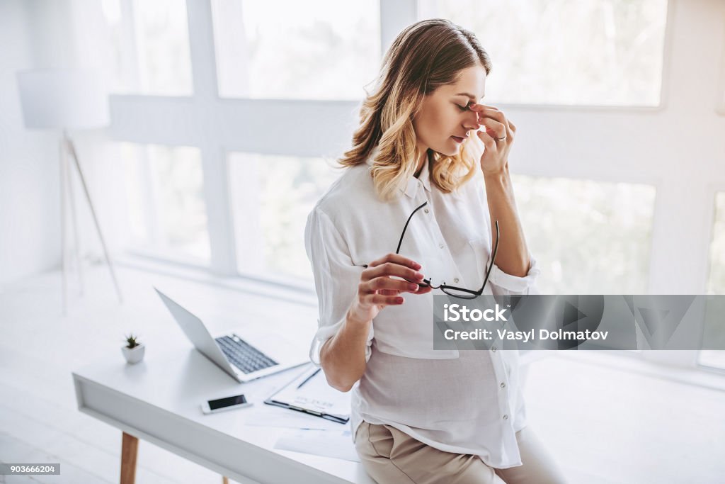 Pregnant woman working Attractive pregnant woman is working in light modern office. Feel of tiredness on last months of pregnancy. Pregnant Stock Photo