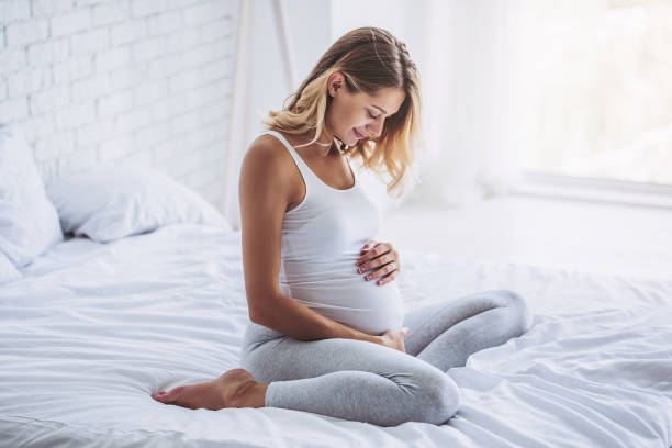 Pregnant in bed. Attractive pregnant woman is sitting in bed and holding her belly. Last months of pregnancy. childbirth photos stock pictures, royalty-free photos & images