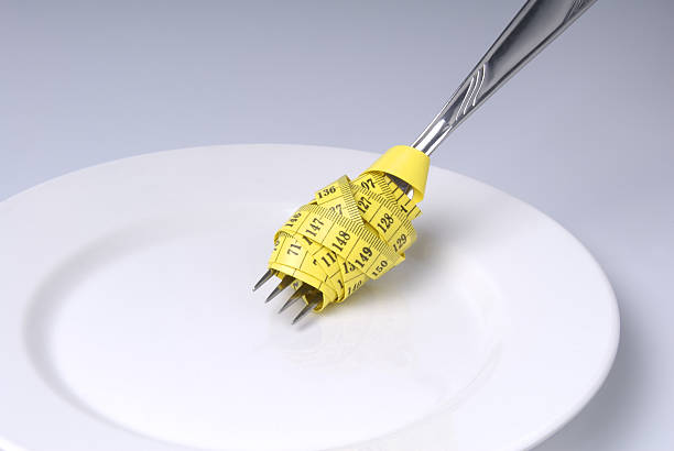 ruban de mesure enroulé autour de fourchette sur une assiette - healthy eating fork tape measure still life photos et images de collection