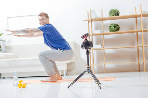 istock Smiling blogger bending his knees in front of a modern camera 903687406