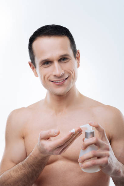 uomo attraente positivo che si prende cura del suo corpo - men smooth the human body moisturizer foto e immagini stock