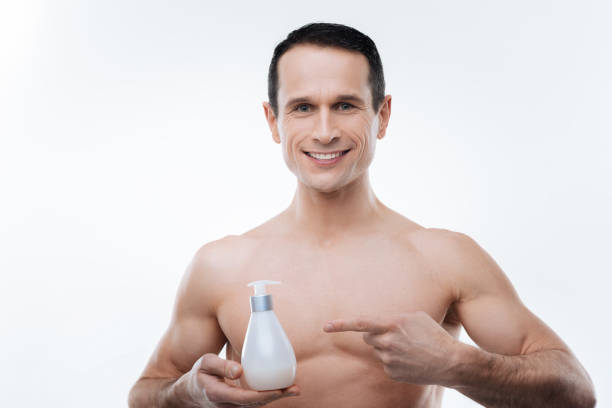 felice uomo positivo che punta alla lozione del corpo - men smooth the human body moisturizer foto e immagini stock