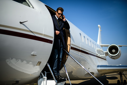 Man wearing elegant clothes exiting the private jet airplane and talking over mobile phone.