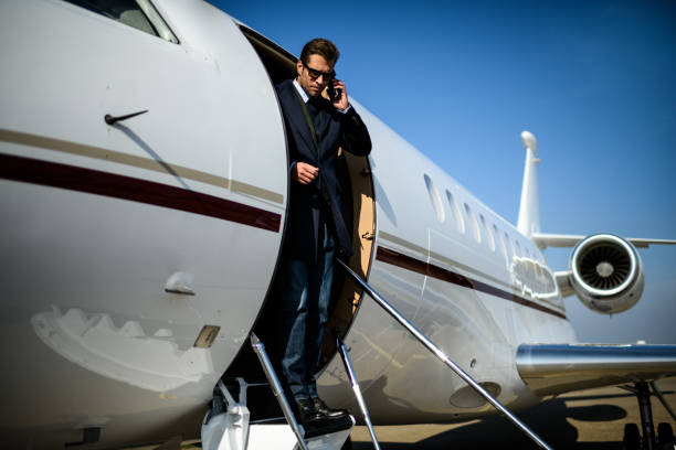 Man at the airport Man wearing elegant clothes exiting the private jet airplane and talking over mobile phone. flight of steps stock pictures, royalty-free photos & images