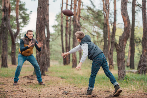 père et fils jouant avec ballon en forêt - throwing football men ball photos et images de collection