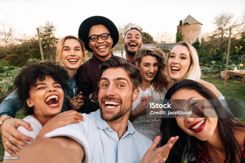 Friends making a selfie together at party Friends chilling outside taking group selfie and smiling. Laughing young people standing together outdoors and taking selfie. Friendship Stock Photo