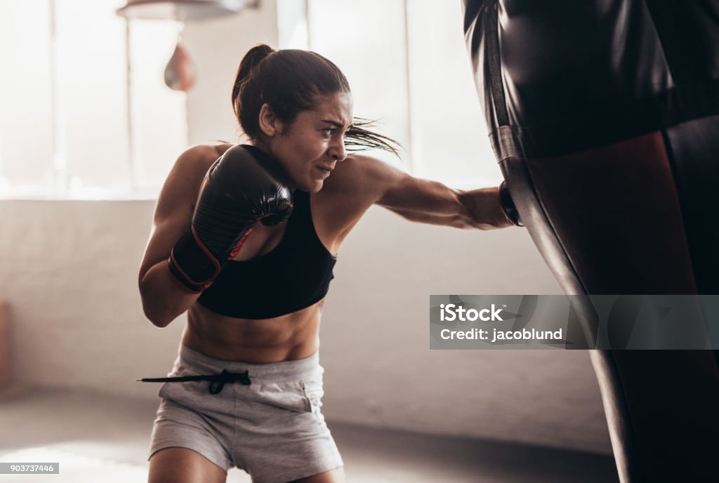 Female boxer training inside a boxing ring Female boxer hitting a huge punching bag at a boxing studio. Woman boxer training hard. Boxing - Sport Stock Photo