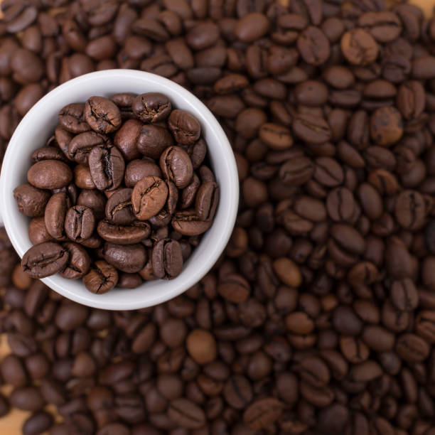 istock Brown coffee beans background with a full white espresso coffee cup 903742306