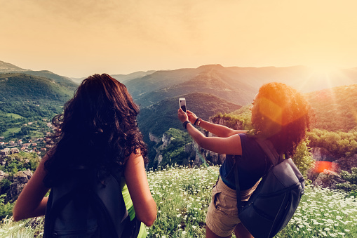 Young women hiking in the mountain and taking photos on sunset
