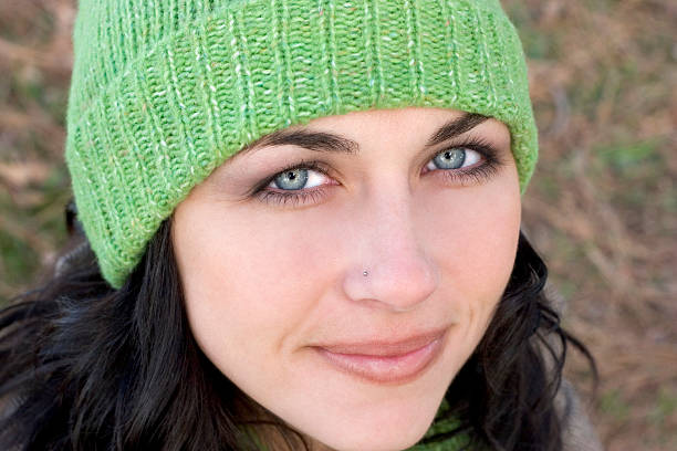 A close-up image of a woman with curly hair, dressed in a blue sweater and a green beret, standing against a solid green background. She has a confident and thoughtful expression, with her hand touching her chin while she smiles. Her round glasses add a touch of intellectual charm to the photograph. The image beautifully captures a moment of self-assurance and pleasant contemplation, making it perfect for themes related to confidence, thoughtfulness, and positive self-expression.