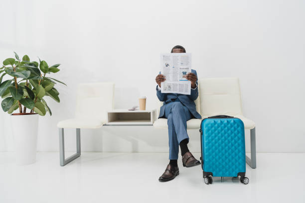 Businessman reading newspaper African american Businessman sitting in waiting room and reading newspaper newspaper airport reading business person stock pictures, royalty-free photos & images