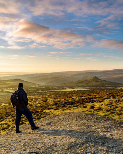 Walker viewing sunrise over Sharp Tor, Dartmoor, UK Photograph of Walker viewing sunrise over Sharp Tor, Dartmoor, UK dartmoor photos stock pictures, royalty-free photos & images
