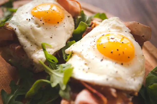 Photo of Fried eggs sunny side up on baguette, ham and arugula