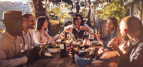 Young multi-ethnic friends dining at rustic countryside restaurant at sunset Young elegant multi-ethnic friends celebrating and having mediterranean lunch at rustic countryside mountain village house cyprus island photos stock pictures, royalty-free photos & images