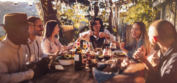 Young multi-ethnic friends dining at rustic countryside restaurant at sunset Young elegant multi-ethnic friends celebrating and having mediterranean lunch at rustic countryside mountain village house rich black men pictures stock pictures, royalty-free photos & images