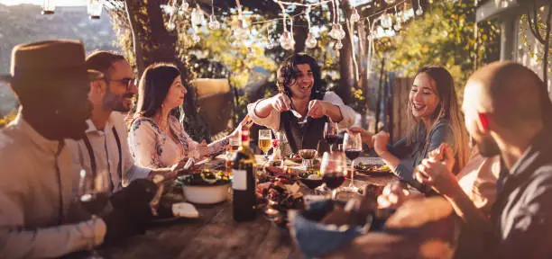 Photo of Young multi-ethnic friends dining at rustic countryside restaurant at sunset