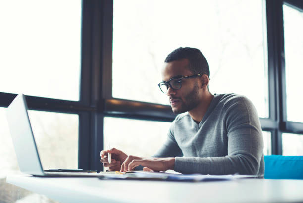 istock Concentrated businessman checking accounting documentation in online database on modern computer connecting to wireless internet connection. Male aro american entrepreneur working on laptop indoors 903783602