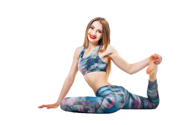 young beautiful woman in color-blue top and leggings yoga posing isolated over white studio background and looking at camera