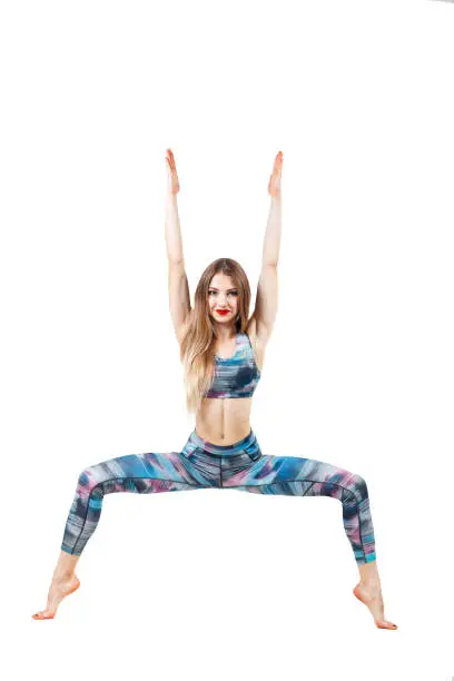 young beautiful woman in color-blue top and leggings practicing yoga, standing in Chair exercise, doing Utkatasana pose, isolated over white studio background and looking at camera