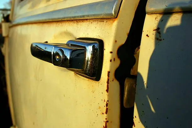A close up image of the door handle and door of a broke down volkswagen beetle.