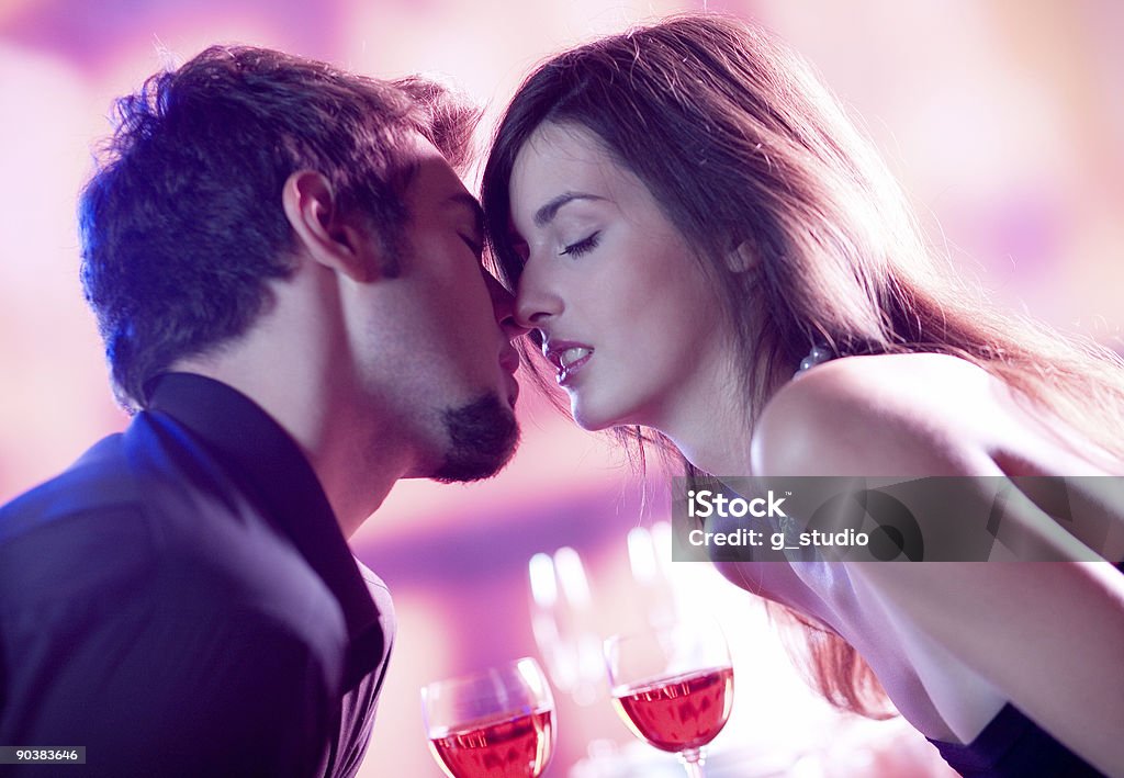 Young couple drinking red wine leaning in for a kiss Young kissing couple celebrating with red wine together Adult Stock Photo