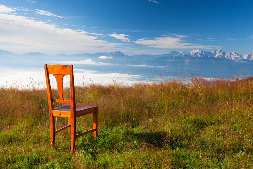 Old wooden chair on the top in Carnic Apls in Austria.Inverse weather and view of the mountains in Slovenia.