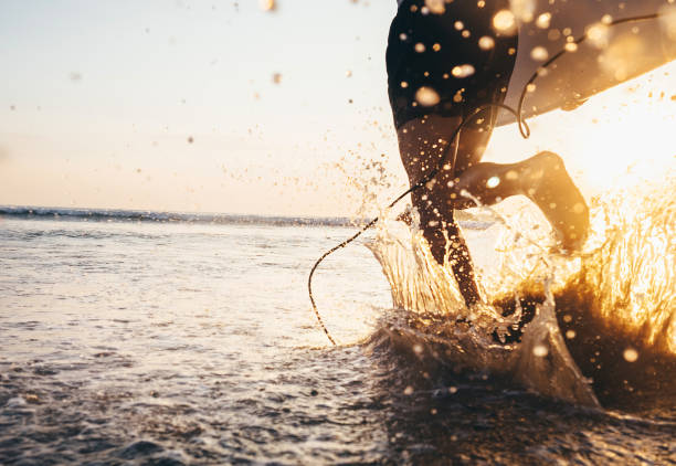 istock Man surfer run in ocean with surfboard. Closeup image water splashes and legs, sunset light 903842974