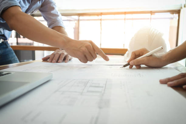 istock Image of engineer or architectural project, Close up of Architects engineer's hands drawing plan on BluePrint and discussing to partner with Engineering tools on workplace, Construction concept 903843200