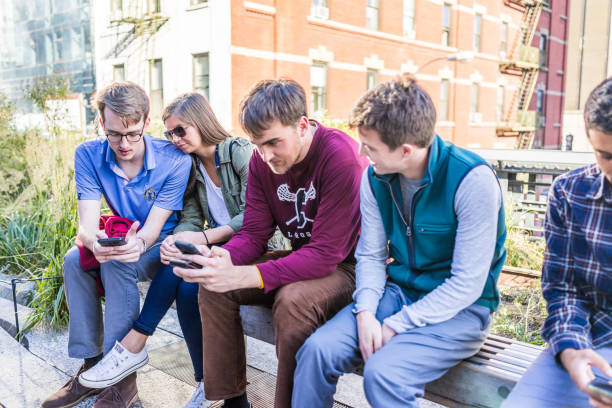 primo piano di giovane coppia con gli amici che guardano gli smartphone, telefono seduto in panchina nel moderno parco di giardino urbano di linea alta a new york city a chelsea west side di hudson yards - 5547 foto e immagini stock