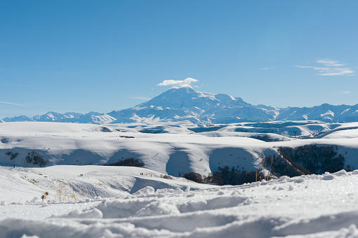 The landscape of snow-covered Caucasian rocks on the Gumbashi Pass. Sleeping Elbrus Volcano and the main Caucasian ridge