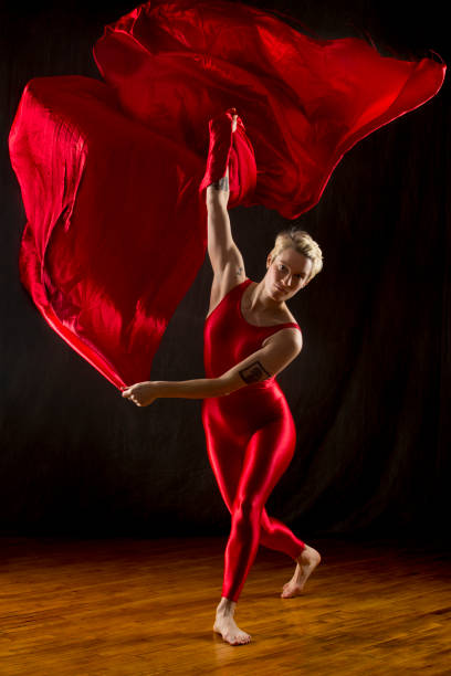 istock Young woman in red unitard swirling red fabric in studio. 903884432