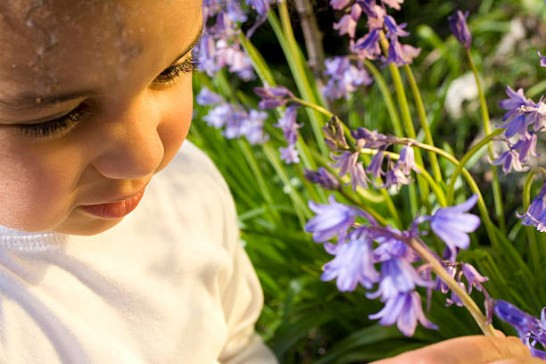 A girl with a yellow hairpin and a yellow scarf holds a purple bouquet of hyacinths in hands