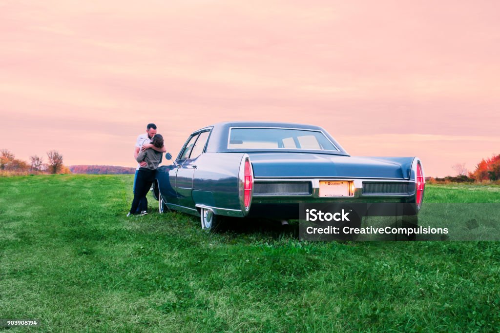 Blue Fleetwood Cadillac 1967 parked at sunset in a field The driver and his girlfriend are parked in a field to watch the burning red sunset fall on the distant forest.  Green grass and a purple pink sky wrap the vehicle in an evening glow.  An old car with its manufacturer’s blue paint, pimped up by the driver, drives and looks like new. 1967 Stock Photo