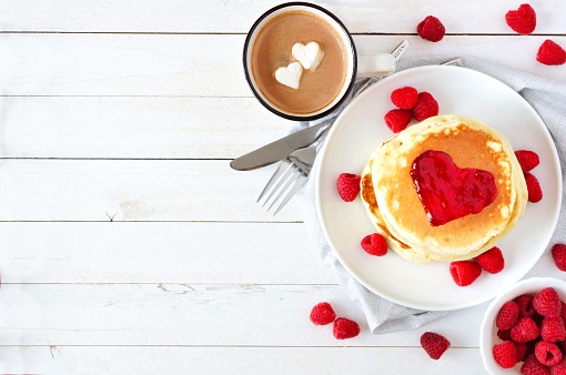 Love concept breakfast with pancakes, hot chocolate and raspberries over white wood