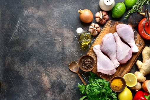 Raw organic chicken legs with ingredients for cooking (marinating) on a wooden cutting board over dark slate, stone or concrete background.Top view with copy space.