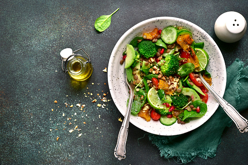 Detox spring salad from green vegetables (avocado, cucumber, broccoli and baby spinach) on a plate over light slate, stone or concrete background.Top view.