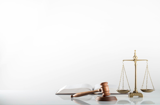 A gavel rests in front of a row of law books in a contemporary law office that looks out toward a big city as the late afternoon sun filters in through the windows.