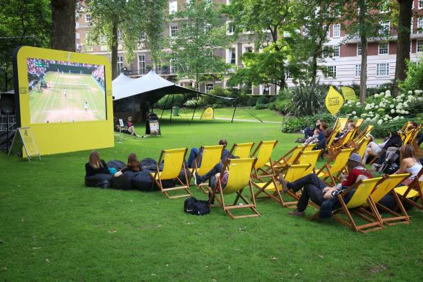 Wimbledon broadcast London: People enjoy public Wimbledon tennis tournament broadcast in Grosvenor Square park of London, UK. wimbledon seats stock pictures, royalty-free photos & images