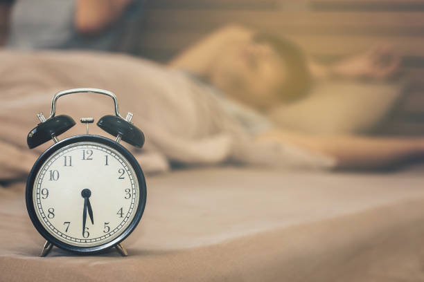 istock Close-Up Of Alarm Clock By Man Sleeping On Bed 903984528
