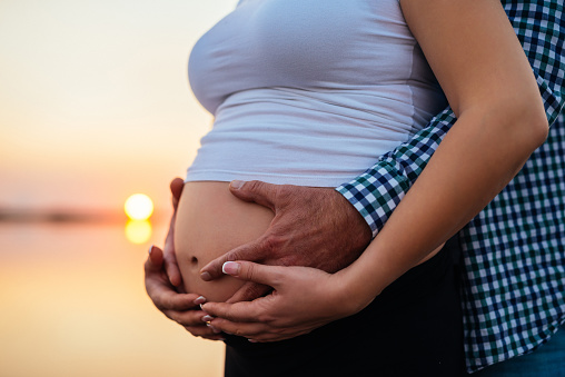 Man holding woman's pregnant belly outdoors on a sunset.