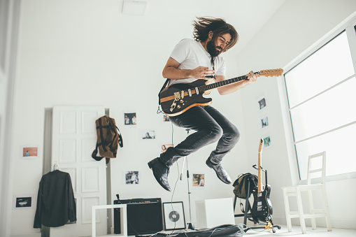 One man, playing guitar and jumping alone, in home studio.
