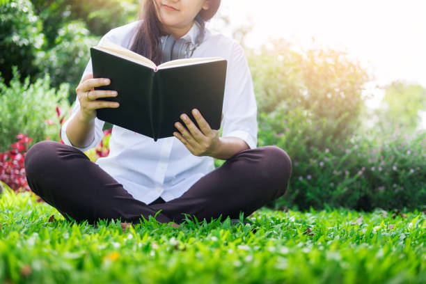 istock Low Section Of Woman Reading Book While Sitting On Grassy Field At Park 903993576