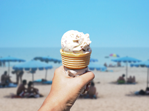 hand holding ice cream cone over summer beach background.