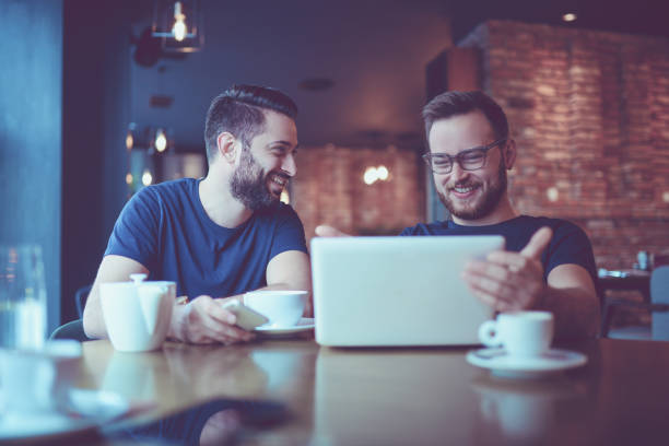 istock Two Smiling  Male Freelancers Drinking Coffee and Video Conferencing In Coffee Restaurant 904008460