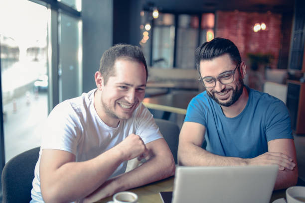 istock Two Smiling  Male Freelancers Drinking Coffee and Video Conferencing In Coffee Restaurant 904011760