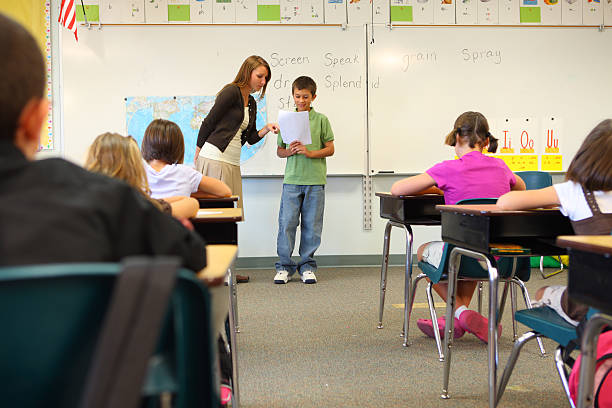 Over the shoulder view of a teacher teaches a group of teenagers in a classroom